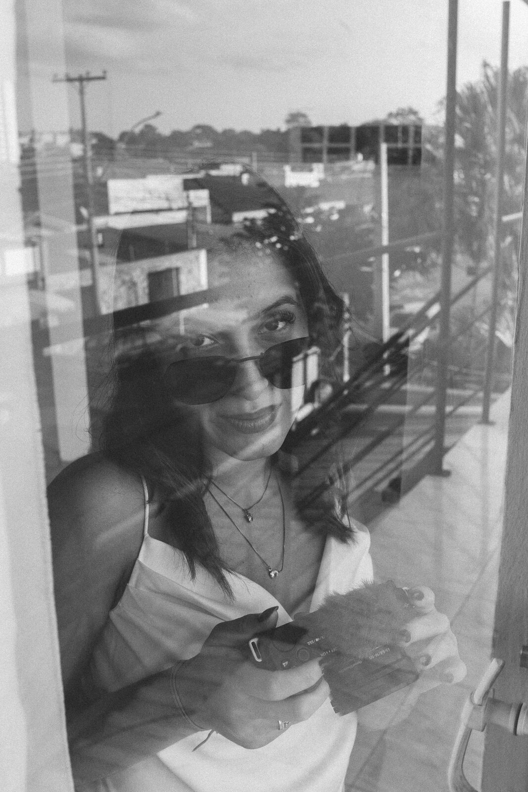 Julia em retrato editorial, refletida na janela com a cidade ao fundo